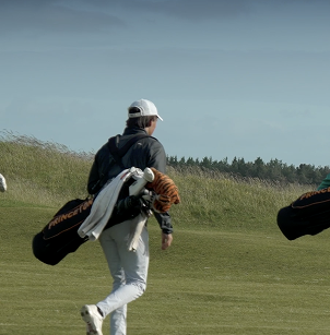 man walking on green field carry golfing bag