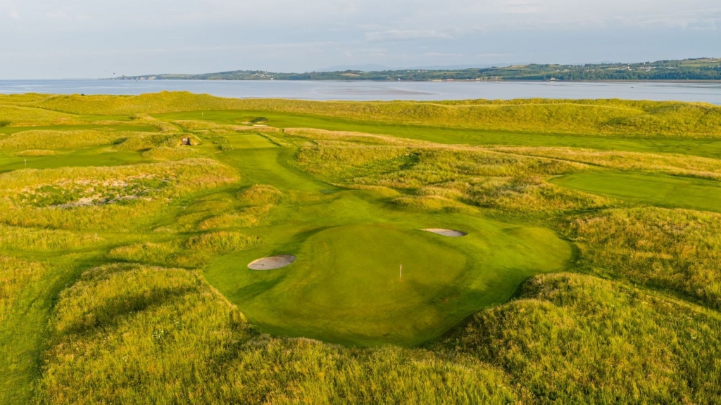 aerial view of the fairway and green with two sand dunes and coastal views