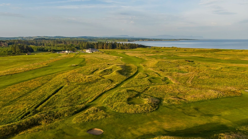 Golf course fairway and green surrounded by tall dunes and forestry in the background.